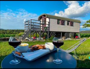 a table with two glasses of wine and a house at La roulotte belle fleur in Saint-Nabord