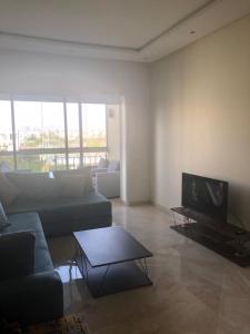 a living room with a couch and a tv at Bel appartement pied sur mer vue imprenable sur piscine et jardins in Sidi Rahal