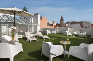 patio z białymi krzesłami, stołami i parasolem w obiekcie Suites Sevilla Plaza w Sewilli