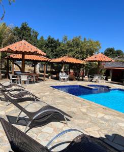 uma piscina com cadeiras, mesas e guarda-sóis em Pousada Encanto dos Anjos em Pirenópolis