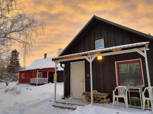 a black house in the snow with a red barn at Self Check-in Sauna Cabin next to Hiking Trails in Kärde