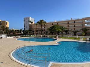 two swimming pools with people in them in front of a building at Achacay Sunset Apartment in Los Cristianos