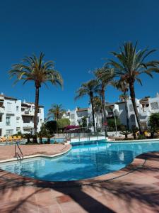a swimming pool with palm trees and buildings at Espectacular apartamento primera linea de playa - Golf in Estepona