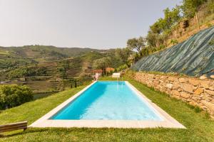 a swimming pool in the middle of a field with a stone wall at DouroParadise in Peso da Régua