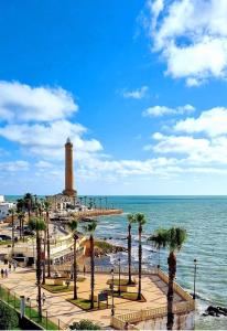 - un phare sur une plage avec des palmiers et l'océan dans l'établissement Hostal Cristina, à Chipiona