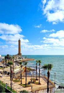 a lighthouse on a beach with palm trees and the ocean at Hostal Cristina in Chipiona