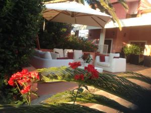 a patio with white chairs and an umbrella and red flowers at Cala Rosa Club Hotel in Stintino
