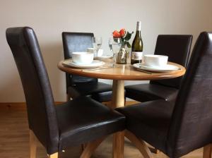 a wooden table with black chairs and a bottle of wine at Morris Gardens Apartments in Oldmeldrum