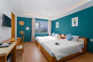 a hotel room with two beds and a desk and a window at Merry Land Hotel Da Nang in Danang
