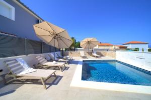 a pool with chairs and umbrellas next to a building at Villa QUARNARO with heated pool in Omišalj
