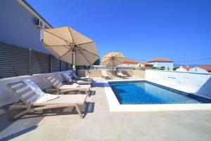 a swimming pool with chairs and umbrellas on a patio at Villa QUARNARO with heated pool in Omišalj