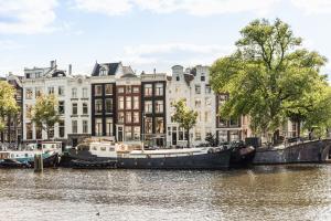 een groep boten aangemeerd op een rivier voor gebouwen bij Studio next to Skinny Bridge near Rembrandtsquare in Amsterdam