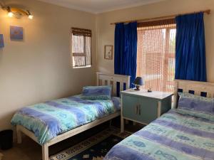 a bedroom with two beds and a window with blue curtains at Smitsand Holiday home in Witsand