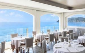 un restaurante con mesas y sillas blancas y ventanas grandes en Grand Hotel Spiaggia, en Alassio
