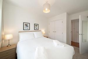 a white bedroom with a large white bed and a lamp at At The Links in Carnoustie