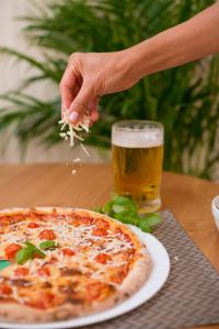 a person sprinkling cheese on a pizza with a glass of beer at Seva Hotel Health Club in Campina