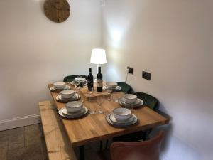 a wooden table with plates and wine glasses and a clock at Rose Cottage. Family home on the river in Hawes
