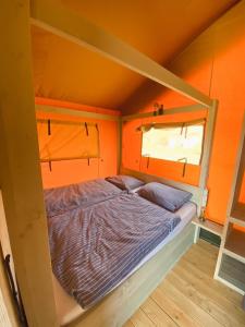 Cama en habitación con pared de color naranja en camping?glamping morskersweitje en Winterswijk