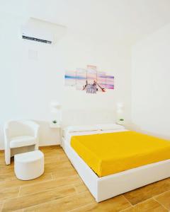 a white bedroom with a yellow bed and a chair at Sea Dream in Agropoli