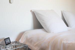 1 cama con sábanas blancas y mesa auxiliar con reloj despertador en La Vedrenne Grange connectée à Limoges en Bonnac-la-Côte