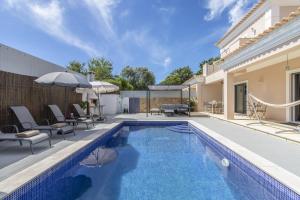a pool with chairs and umbrellas next to a house at Villa Maya by Algarve Holidays in Almancil