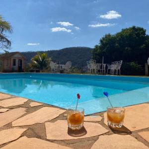 dos bebidas sentadas en una mesa junto a una piscina en Pousada 2 Baioco, en Paty do Alferes