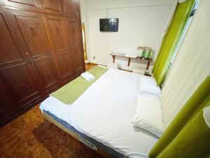 1 dormitorio con 1 cama blanca grande con cortinas verdes en Pousada e Hospedaria Regina, en Cachoeiro de Itapemirim