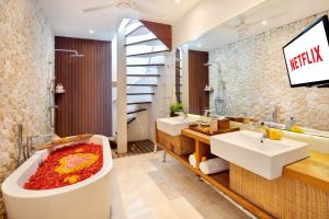 a bathroom with two sinks and a tub with a tv on the wall at The Jimbaran Villa by Ini Vie Hospitality in Jimbaran