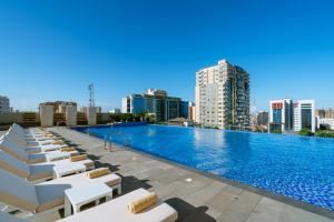 une grande piscine avec des chaises blanches et des bâtiments dans l'établissement Johari Rotana, à Dar es Salaam