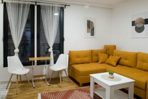 a living room with a yellow couch and white chairs at Apartmani Pijemont in Višegrad