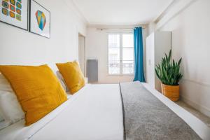 ein weißes Bett mit gelben Kissen in einem Zimmer mit Fenster in der Unterkunft Appartements Bergère in Paris