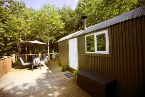 a cabin with a deck with a bench and an umbrella at Riverwood Farms Shepherds Hut in Talaton