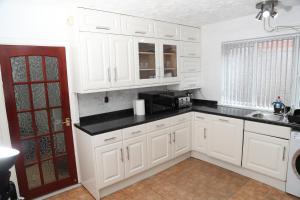 a kitchen with white cabinets and a black counter top at cosy 3-bed bungalow nec airport close to amenities in Birmingham