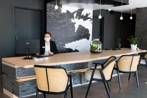 Hostellerie de la Pointe Saint-Mathieu - SPA & Restaurant في بلوغونفولان: امرأة ترتدي قناع الوجه تجلس في مكتب