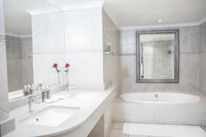 a white bathroom with two sinks and a tub at Indaba Hotel, Spa & Conference Center in Johannesburg