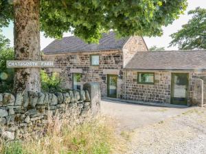 an old stone building with a stone wall and a tree at The Barn at Chatsworth Farm in Leek