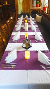 Hotel und Restaurant Nehrener Hof في Nehren: طاولة طويلة مع المناديل الأرجوانية والبيضاء والفضيات