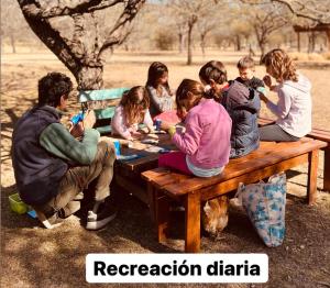 a group of people sitting around a picnic table at Casas de Campo Henin Ecovilla & recreación infantil in Villa General Belgrano