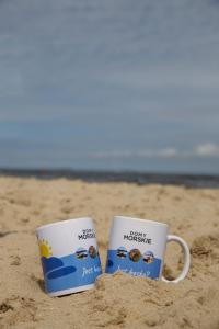 two coffee mugs sitting in the sand on the beach at Domy Morskie Dog Friendly in Jantar