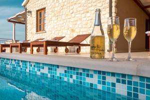 eine Flasche Wein und zwei Gläser neben einem Pool in der Unterkunft Seafront Stone Villa in Blato