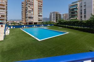 a large swimming pool on a lawn with tall buildings at Travel Habitat playa Heliópolis in Benicàssim