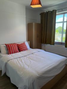 uma cama branca com almofadas vermelhas num quarto em 3 bedroom house in Sutton em Morden