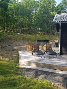 a deck with three chairs and a fire pit at Stuga (Cottage) ålaryd in Skillingaryd