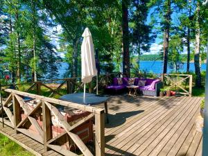 una terraza de madera con sombrilla y sillas moradas en Charmig stuga av rustik stil i Stockholms område, en Estocolmo