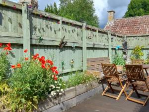 eine Terrasse mit zwei Stühlen und einem Zaun mit Blumen in der Unterkunft Greenham Cottage in Chiselborough