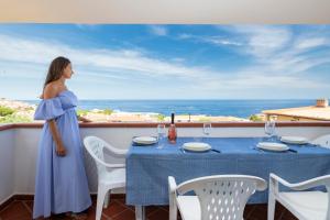 a woman in a blue dress standing on a balcony with a table at Biriola EcoResort Cala Gonone in Cala Gonone