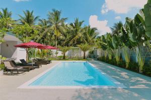 a swimming pool with chairs and umbrellas and palm trees at La villa de CoCo Bến Tre in Ben Tre