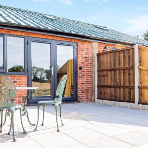 a patio with two chairs and a table and a building at Muntjac View, Beechcroft Barns, Cawston, Norfolk in Norwich