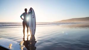 un hombre de pie en la playa con una tabla de surf en Hyatt Regency Taghazout en Taghazout