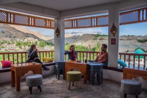 three people sitting at tables in a room with a view at Black Sheep Bed & Breakfast in Kargil